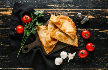 Lezzetli cheburekler, otlar ve domatesler koyu ahşap arka planda, üst manzara