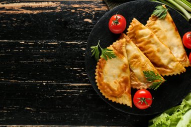 Lezzetli cheburekler, otlar ve domatesler koyu ahşap arka planda, üst manzara