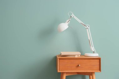 Yeşil duvarın yanındaki masada parlayan lamba.
