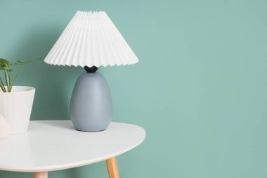 Yeşil duvarın yanındaki masada bitki olan şık bir lamba.