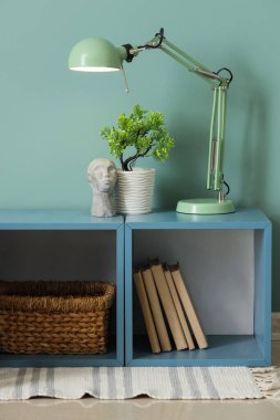 Yeşil duvarın yanındaki rafta bitki ve dekor bulunan şık bir lamba.