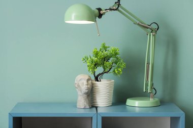 Yeşil duvarın yanındaki rafta bitki ve dekor bulunan şık bir lamba.