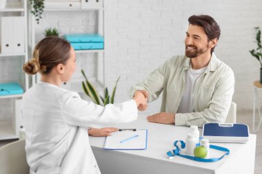 Klinikteki masada beslenme uzmanı olan genç bir adam el sıkışıyor.