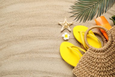 Plaj ayakkabılarıyla kompozisyon, güneş kremi şişesi ve arka plan olarak kum üzerinde hasır çanta, yakın plan.