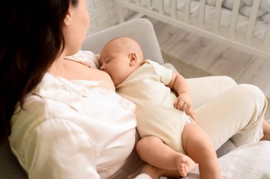 Genç bir kadın evdeki koltukta bebeğini emziriyor.