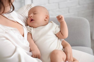 Genç bir kadın evdeki koltukta bebeğini emziriyor.