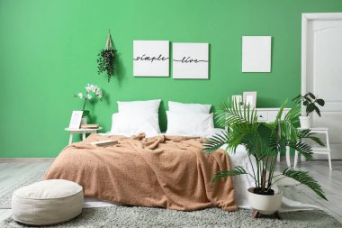 Yatak odasının içinde masalar, tablolar ve yeşil bitkiler var.