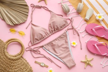 Pembe arka planda şık mayo, kulaklık ve plaj aksesuarlarıyla kompozisyon, yakın plan.