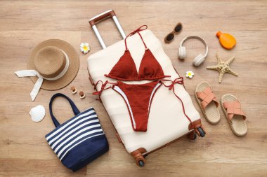 Bavul, şık mayo ve plaj aksesuarları ahşap zeminde, yakın plan.