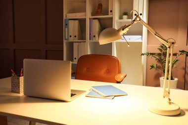 Geceleri ofiste dizüstü bilgisayarı ve parlayan lambası olan bir iş yeri