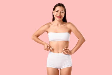 Pembe arka planda selülit sorunu olan iç çamaşırlı genç bir kadın.