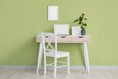 Ofisteki yeşil duvarın yanındaki masada güzel bir Anthurium çiçeği ve boş bir laptop.