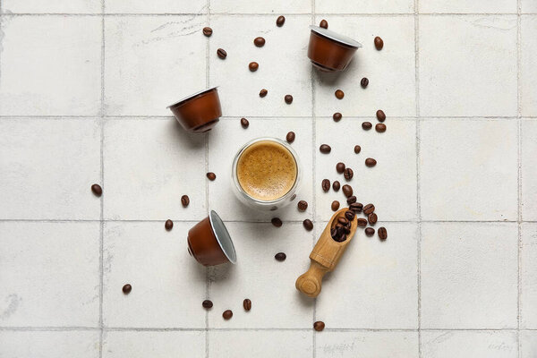 Cup of delicious espresso, pods and beans on white tiled table