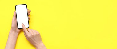 Sarı arka planda cep telefonu olan kadın eller