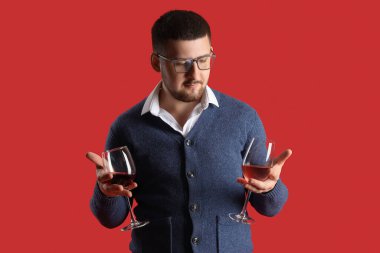 Genç şarap garsonunun elinde kırmızı arka planda farklı türde şarap bardakları var.