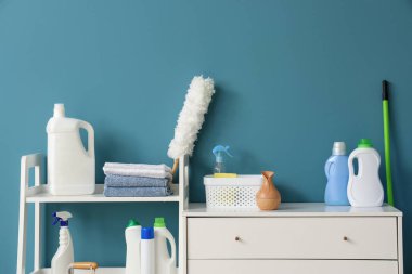 Mavi duvarın yanında temizlik malzemeleri olan bir dolap.