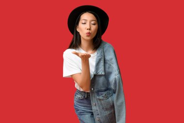 Şık kot elbiseli güzel bir Asyalı kadın kırmızı arka planda öpüşüyor.