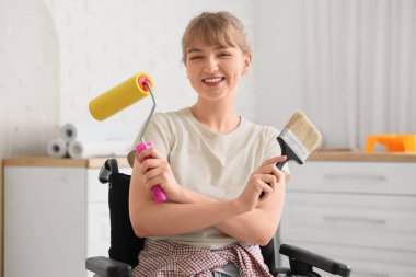 Tekerlekli sandalyedeki genç kadın evde boya fırçası ve silindirle geziyor.