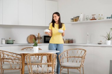 Modern mutfaktaki yemek masasına çaydanlık ve çay koyan genç bir kadın.