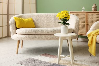 Modern oturma odasının içinde rahat bir kanepe, sehpada çiçekler ve yastıklı vazo.