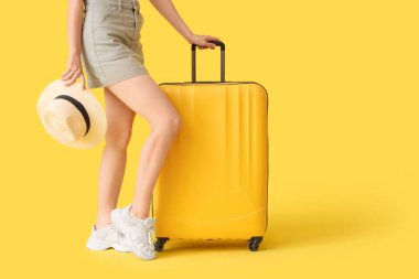 Sarı arka planda bavulu ve şapkası olan genç bir kadın.