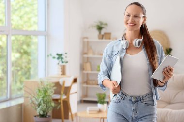 Evde dizüstü bilgisayarı ve tableti olan genç bir kadın var.