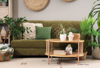 Oturma odasının içinde yeşil kanepe, masa ve bitkiler var.