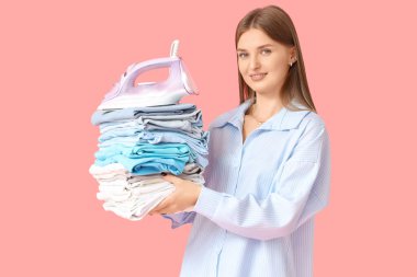 Pembe arka planda bir yığın elbisesi ve demiri olan genç bir kadın.