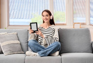 Evdeki kanepede oturan e-okuyuculu genç kız.