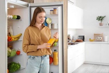 Mutfaktaki açık buzdolabının yanında meyve suyu şişesi olan genç bir kadın.