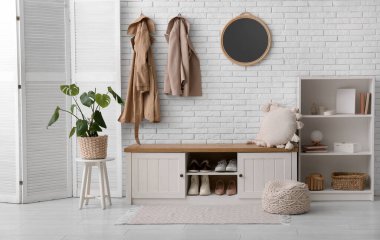 Folding screen, houseplant and bench near white brick wall in hallway