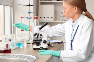 Female scientist with test tube and microscope working in laboratory