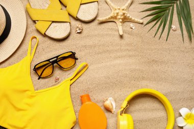 Kadın plaj aksesuarları, bir şişe güneş kremi ve kumdaki kulaklıklar.