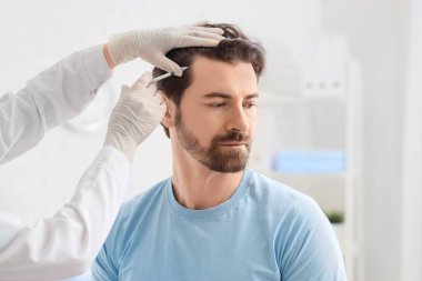 Doktor klinikte saç büyümesi için adama iğne yapıyor.