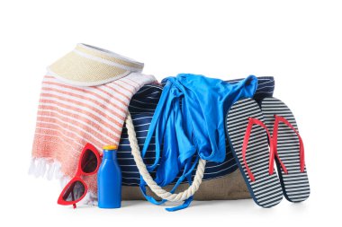 Beyaz arka planda izole edilmiş güneş kremi, mayo ve plaj aksesuarlarıyla dolu bir plaj çantası.