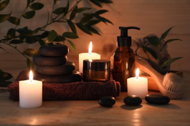 Spa taşları, yanan mumlar, kavanoz ve bir şişe kozmetik ürünü ahşap arka planda, yakın plan