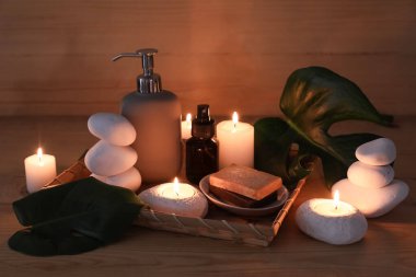Spa taşlı kompozisyon, yanan mumlar ve ahşap arka planda kozmetik ürünlerin şişeleri, yakın plan