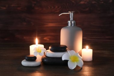 Spa taşlı kompozisyon, yanan mumlar ve ahşap arka planda bir şişe kozmetik ürünü, yakın plan.