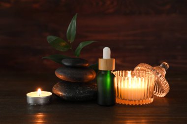 Spa taşlı kompozisyon, yanan mumlar ve ahşap arka planda bir şişe kozmetik ürünü, yakın plan.