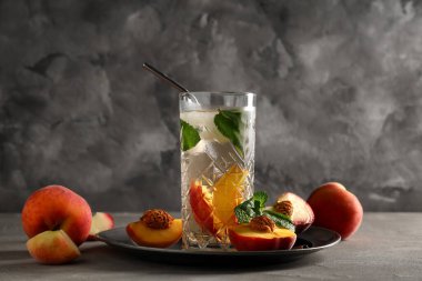 Bir bardak taze şeftalili limonata, nane ve gri arka planda meyveler.