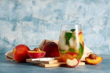 Bir bardak taze şeftalili limonata, nane ve mavi arka planda meyveler.