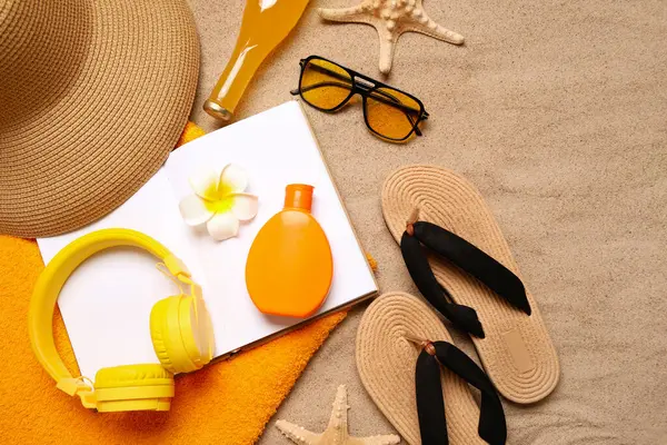 Şık plaj aksesuarları, modern kulaklıklar, kumda defter ve bir şişe içki.