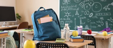 Kitaplı elma, su şişesi ve sırt çantası sınıfın masasında.