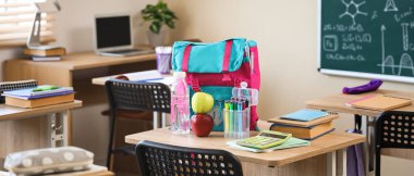 Sınıftaki masada su şişesi ve sırt çantalı elmalar.