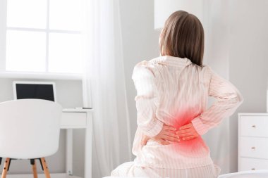 Yatak odasında sırt ağrısı çeken genç bir kadın.