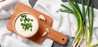 Lezzetli ekşi krema ve gri arka planda dilimlenmiş yeşil soğan tabağı.