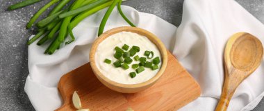 Lezzetli ekşi krema ve gri arka planda dilimlenmiş yeşil soğan tabağı.