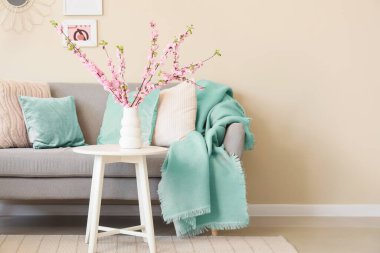 Oturma odasının içinde gri kanepe ve vazoda çiçek açan ağaç dalları var.