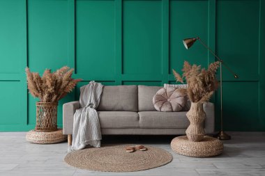 Gri kanepe, puf ve vazolar. Oturma odasının içinde yeşil duvarın yanında çimen var.