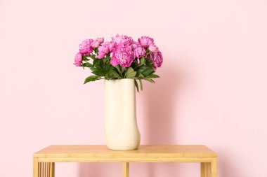 Renk duvarının yanındaki raflarda duran pembe şakayık vazosu.